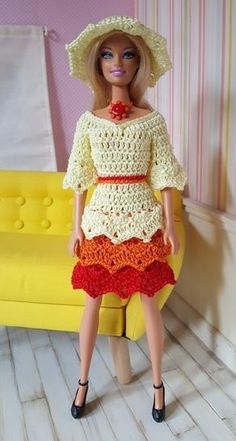 a doll wearing a crocheted dress and hat in front of a yellow couch