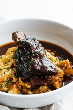 a bowl filled with meat and gravy on top of a white table cloth