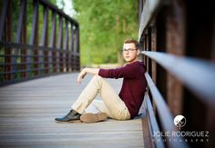 a young man is sitting on a bridge with his legs crossed and looking at the camera