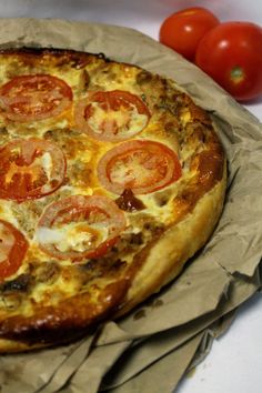 a pizza sitting on top of a piece of wax paper next to tomatoes and a knife