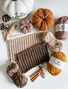 yarn and knitting needles laid out on top of a white surface next to a pumpkin