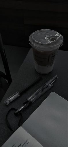 a black and white photo of a cup of coffee next to an open notepad