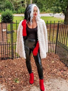 a woman with white hair wearing black and red clothes, standing in front of a fence