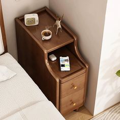 a nightstand with a phone, alarm clock and cup of coffee on it next to a bed