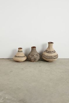 three vases sitting next to each other on a cement floor in front of a white wall