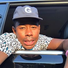 a young man wearing a hat leaning out the window of a car with his hand on the door handle