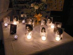 many candles are lit up on a table with pictures and flowers in the background at night