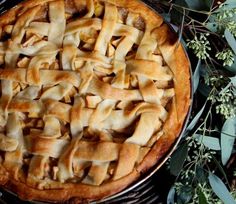 an apple pie sitting on top of a wooden table next to green leaves and flowers