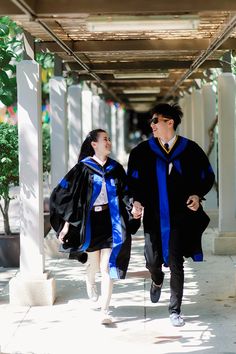 two people in graduation gowns walking down the street together with one person wearing a cap and gown