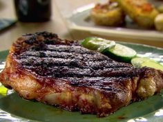 a piece of steak on a plate with potatoes and cucumbers in the background