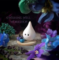 a small figurine sitting on top of a wooden base surrounded by purple and blue flowers