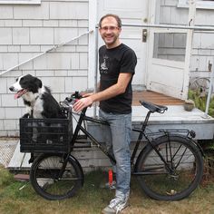 a man standing next to a bike with a dog in the basket on it's front wheel