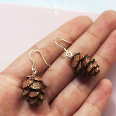 small pine cone earrings are shown on someone's hand