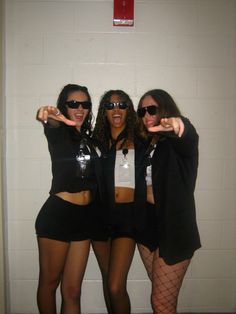 three women dressed in black posing for the camera with their arms around each other and one pointing at the camera