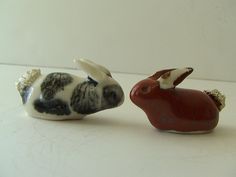 two ceramic rabbits sitting next to each other on a white surface with one rabbit facing the other way