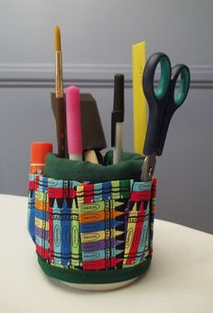 a pencil cup with scissors, pens and markers in it sitting on a white table