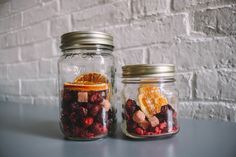 two mason jars filled with dried fruit and orange slices on a table next to a brick wall