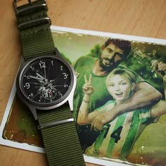 a watch sitting on top of a wooden table next to a card with an image of a man and woman