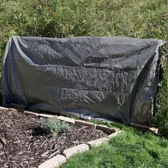 an outdoor covered bench in the middle of some grass and plants with bushes behind it