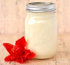 a red flower sitting on top of a table next to a mason jar filled with milk