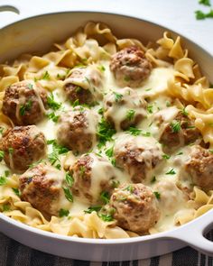 a white dish filled with pasta and meatballs covered in gravy, garnished with parsley