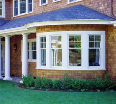 a brown house with white trim and windows on the front porch, grass in front of it