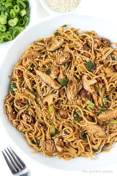 a white bowl filled with noodles and mushrooms on top of a table next to green onions