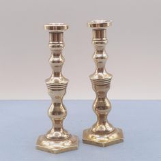 two gold colored candlesticks sitting side by side on a light blue table top