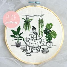 the embroidery pattern shows a woman sitting on a bean bag in front of some potted plants