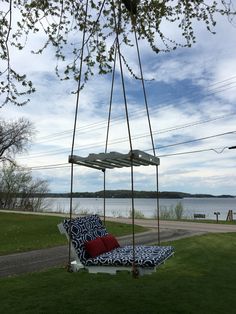 a swing chair sitting on top of a lush green field next to a lake in the background