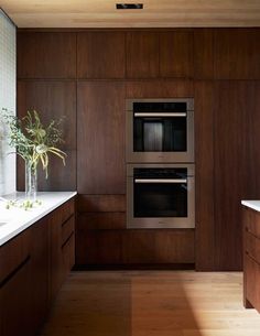 a modern kitchen with wooden cabinets and stainless steel ovens, white counter tops, and wood flooring