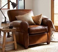 a brown leather chair sitting in front of a window next to a table with a glass of wine on it