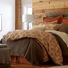 a bed with brown and tan comforters in a bedroom next to a chair, table and lamp