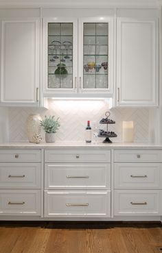 a kitchen with white cabinets and wood flooring, glass front cupboards on the wall