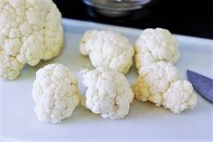 several cauliflower heads on a cutting board with a knife