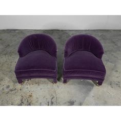 two purple velvet chairs sitting on top of a cement floor in front of a white wall