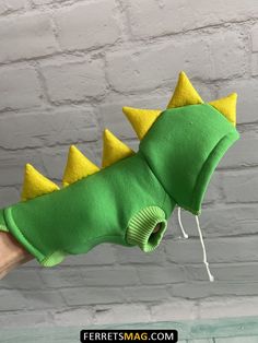 a green and yellow stuffed animal with spikes on it's head is being held by a person