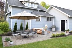 a patio with an umbrella, table and chairs in front of a blue house on a sunny day