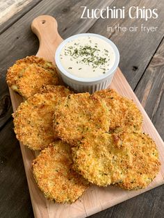 fried zucchini chips on a cutting board with dip in the middle and herbs sprinkled on top