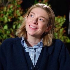 a woman with blonde hair wearing a blue sweater and silver necklace smiling at the camera