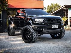 a large black truck parked in front of a building with its lights on and big tires