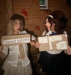 two girls holding cardboard signs that say i need to pee