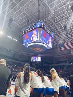 the cheerleaders are lined up in front of the big screen at an indoor basketball game