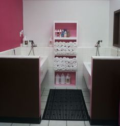 a pink and white bathroom with two sinks, toilet paper roll holders and shelving unit