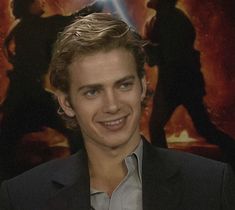 a young man smiling in front of a star wars poster with lightsaben behind him