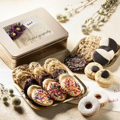 an assortment of cookies and pastries in a tin on a white tablecloth with flowers