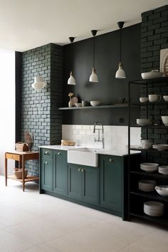 a kitchen with dark green cabinets and white dishes on the counter top, along with black brick walls