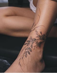 a woman's foot with flowers and leaves tattoo on her left leg, sitting down