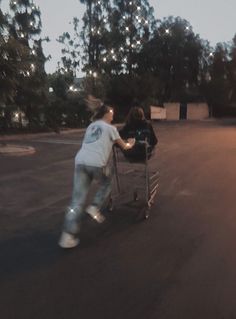 two people pushing a shopping cart down the street at night with trees in the background