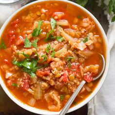 a white bowl filled with vegetable soup and garnished with cilantro leaves